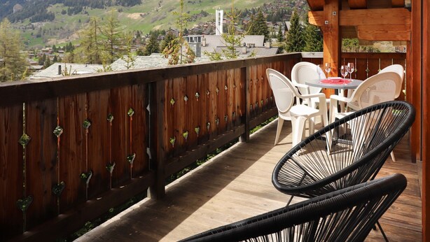 A wooden deck with white chairs and a table, overlooking a mountainous landscape with a church and houses. - Boule de Neige by Interhome (Verbier)