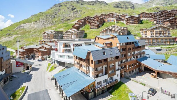 Un hôtel moderne à plusieurs étages, doté d’un parking et offrant une vue sur un paysage montagneux en arrière-plan.