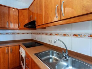 Une cuisine avec des meubles en bois, une cuisinière noire et un évier en acier inoxydable.