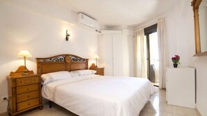 A neatly arranged bedroom with a wooden bed, bedside tables with lamps, a small potted plant, and a window with curtains. - Calpemar by Interhome (Calpe/Calp)