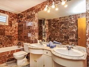 Un bagno con pareti in marmo, una vasca, due lavabi e un water.