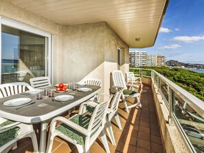 Un balcone con tavolo apparecchiato per mangiare, sedie e vista sul mare e sugli edifici.
