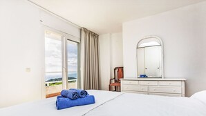 Ein Hotelzimmer mit einem Bett, einem Schminktisch, einem Sessel und einem großen Fenster mit Blick ins Freie.