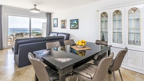 Ein moderner Essbereich mit einem schwarzen Tisch, sechs Stühlen und einer Obstschale. Ein Sofa und ein Balkon mit Meerblick vorhanden.