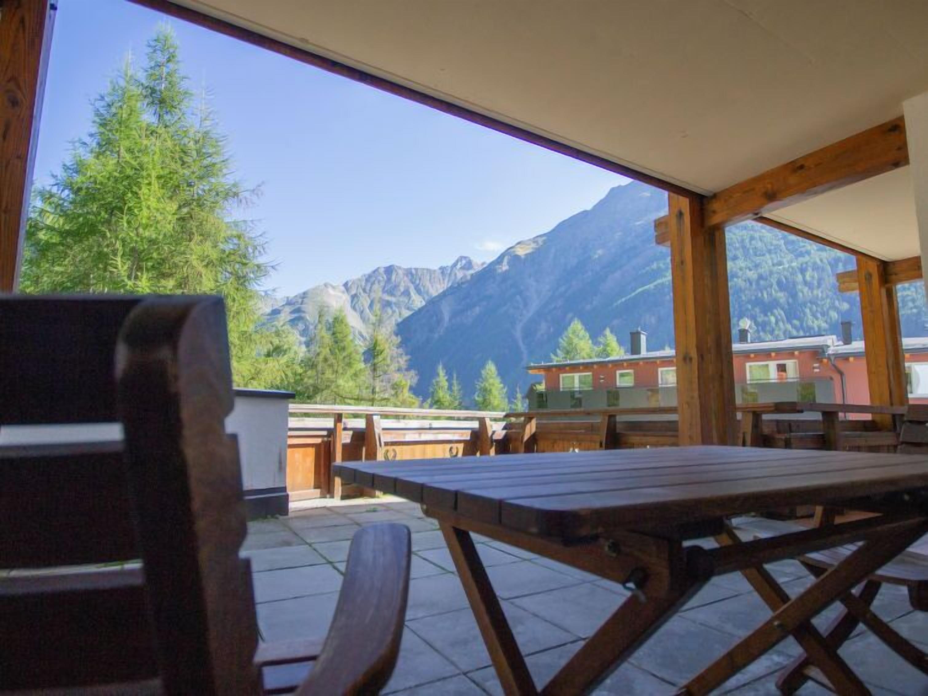 A wooden table and chairs in a room with large windows overlooking a mountain landscape.