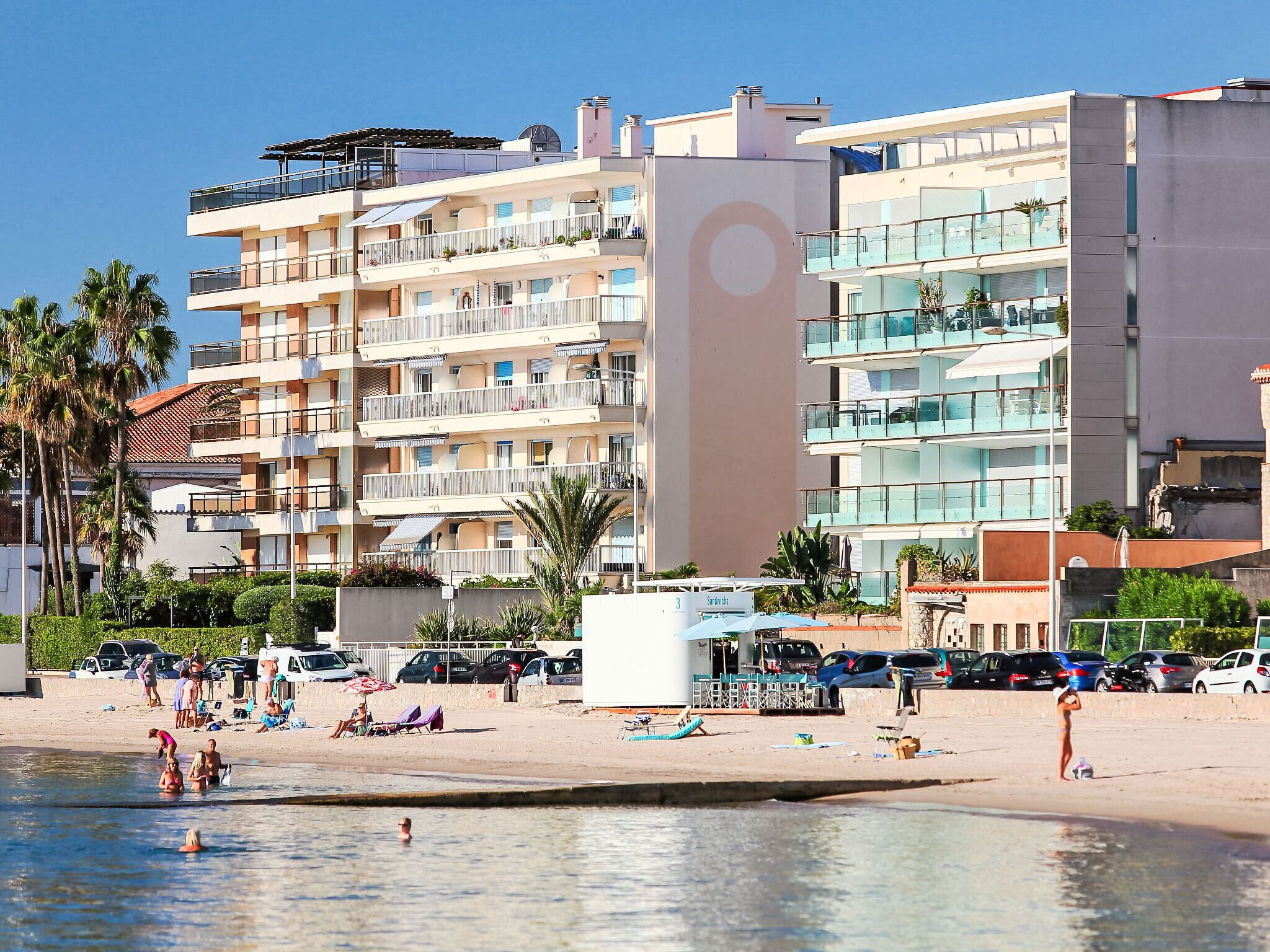 A beachfront hotel with multiple balconies, a swimming pool, and a beach area with people and sun loungers.