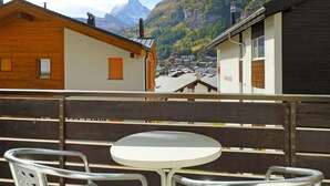 A balcony with a round table and two metal chairs, overlooking a village with houses and mountains in the background. - Apartment Apollo by Interhome (Zermatt)
