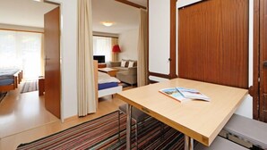 A hotel room with a bed, a desk with a book, a sofa, and a TV in the background. - Apartment Apollo by Interhome (Zermatt)