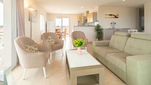 Een moderne woonkamer met een bank, twee fauteuils, een salontafel en een eethoek op de achtergrond.