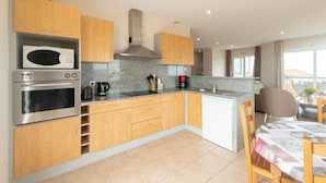 Een moderne keuken met houten kastjes, roestvrijstalen apparatuur en een eethoek met een tafel en stoelen.