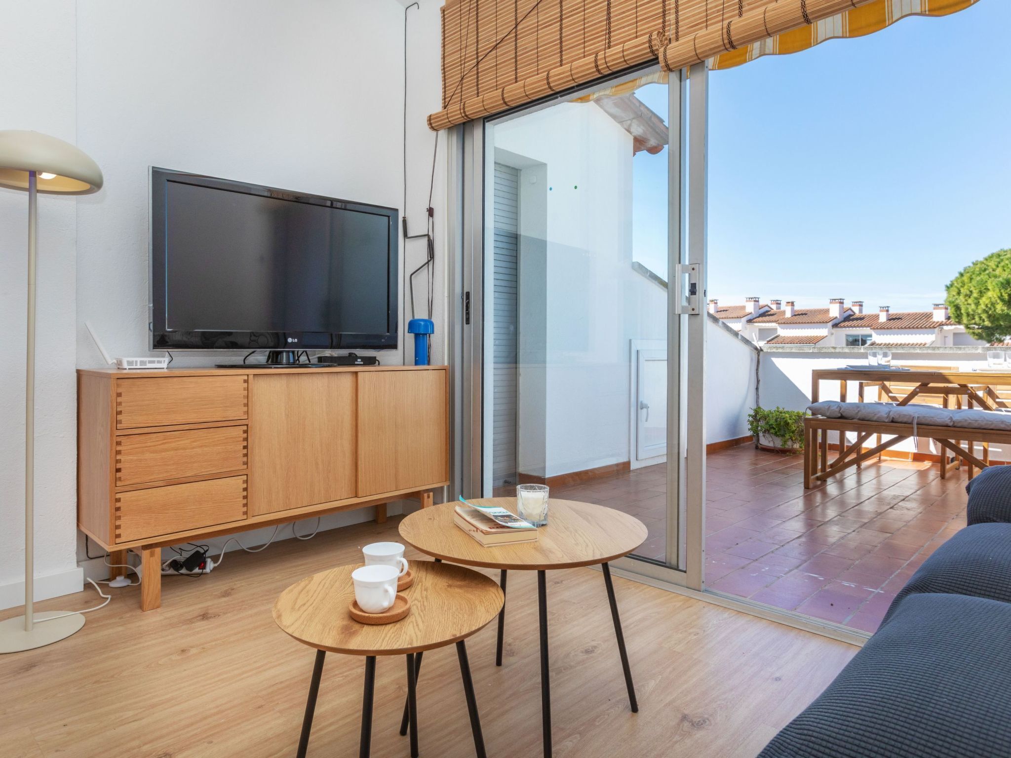 A modern living room with a flat-screen TV, wooden furniture, and a sliding glass door leading to an outdoor terrace.