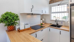 A modern kitchen with white cabinets, a wooden countertop, a built-in oven, a coffee maker, and a window with a view. - Residencial Gran Sol by Interhome (L'Escala)