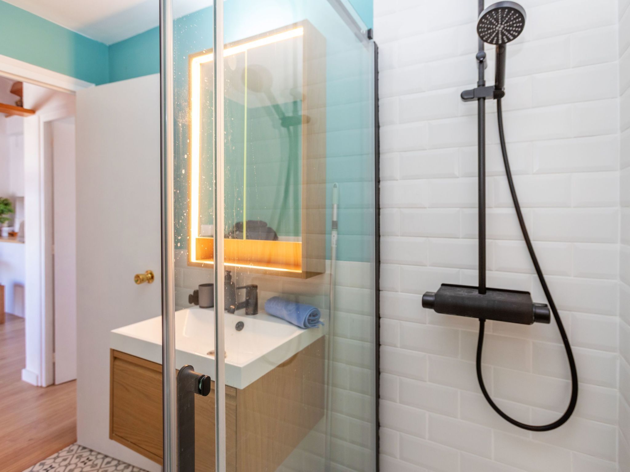 A bathroom with a glass shower enclosure, a white sink, and a mirror with a light.