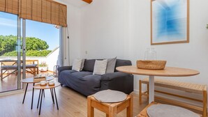 A modern living room with a sofa, coffee table, and chairs, a large window with blinds, and a framed abstract painting on the wall. - Residencial Gran Sol by Interhome (L'Escala)