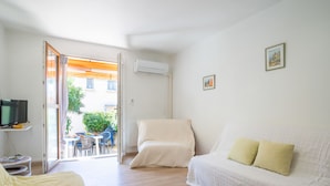 Une pièce comprenant un lit, un canapé, une télévision et une table avec des chaises. Il y a une fenêtre avec des rideaux et un appareil de climatisation fixé au mur.