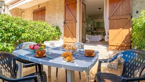 Un espace de restauration en plein air avec une table dressée pour le petit-déjeuner, comprenant des fruits, du pain et des tasses.