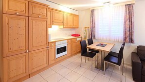 Een compacte keuken met houten kastjes, een inbouwoven en een eethoek met een tafel en stoelen.