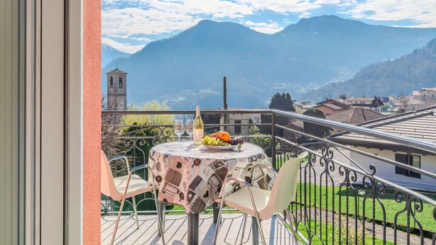 A balcony with a table set for two, overlooking a mountainous landscape with a church tower. - Apartment Marta by Interhome (Cerano d'Intelvi)