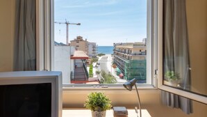Habitación con un amplio ventanal con vistas a la costa, un escritorio con lámpara y un televisor.