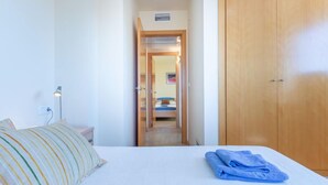Habitación de hotel con cama, escritorio con lámpara, armario y baño visible a través de una puerta abierta.
