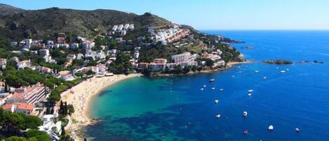 A coastal town with a beach, clear blue waters, and buildings with red-tiled roofs.