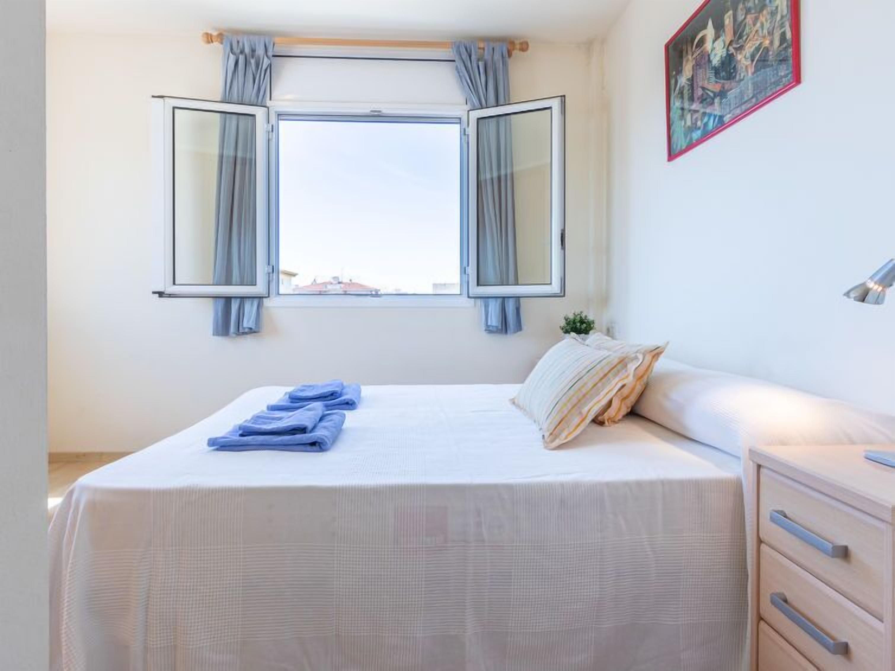 Quarto com cama, mesa de cabeceira, janela com cortinas e um quadro na parede.