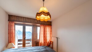 Une chambre avec un grand lit, une tête de lit en bois, une fenêtre avec des rideaux et une vue sur la montagne.