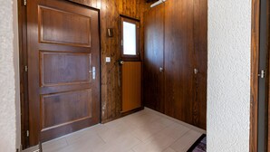 Une porte en bois avec une fenêtre, un mur blanc à texture et un sol carrelé.