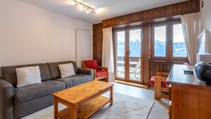 Un salon chaleureux avec un canapé, une table basse en bois et une vue sur les montagnes, visible à travers de grandes fenêtres.