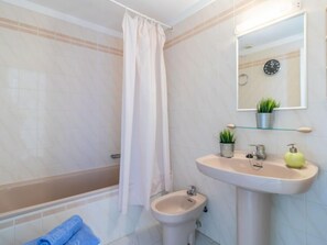 Ein Badezimmer mit einer Badewanne, einem Bidet, einem Waschbecken mit Spiegel und einer Zimmerpflanze.