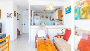 A modern living room with a wooden table and sofa, a kitchen in the background, and a dining area with chairs. - Club Nautic by Interhome (Empuriabrava)