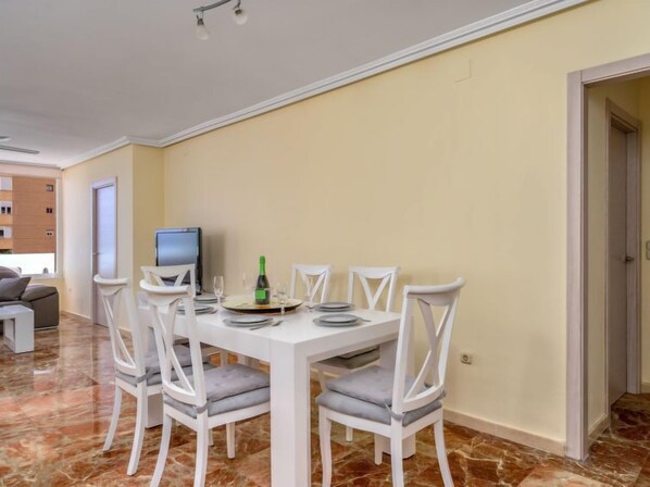 A dining area with a white table set for four, surrounded by white chairs with grey cushions. A bottle of champagne and glasses are on the table. - Playamar by Interhome (Torremolinos)