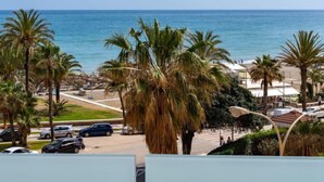 Vista costeira com palmeiras, uma praia e carros estacionados.