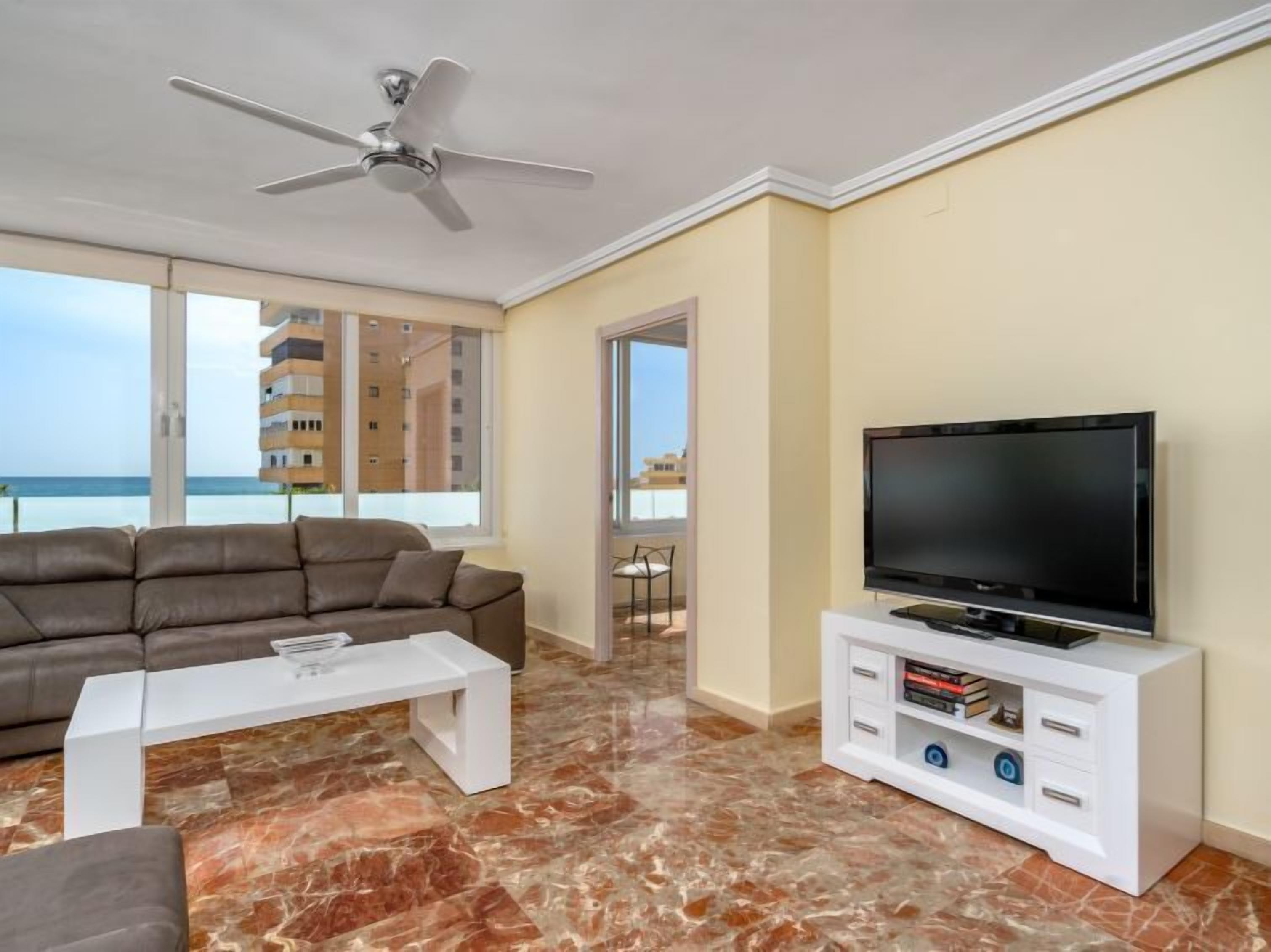 Un saló amb un sofà, una taula de centre, televisió i un ventilador de sostre.