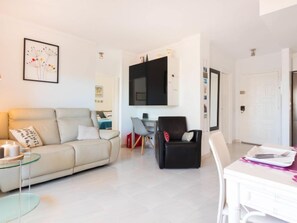 A modern living room with a sofa, a glass coffee table, a dining table with chairs, and a flat-screen TV mounted on the wall. - Club Nautic by Interhome (Empuriabrava)