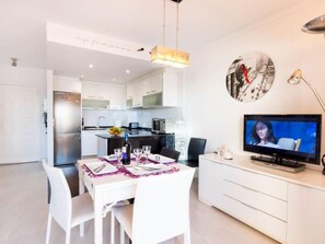 A modern kitchen with white cabinets, a stainless steel refrigerator, and a dining area with a white table set for two. - Club Nautic by Interhome (Empuriabrava)