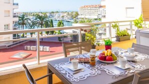 A balcony with a table set for breakfast, overlooking a marina with boats and buildings. - Club Nautic by Interhome (Empuriabrava)