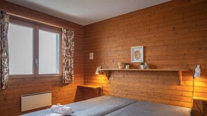 Habitación con dos camas, paredes de madera, una ventana con cortinas, una repisa con objetos decorativos y una lámpara de noche.