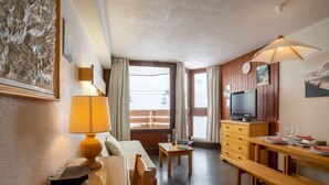 Una habitación acogedora con una mesa de madera, un sofá, un televisor y una mesa de comedor preparada para dos personas.