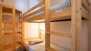 Habitación con literas de madera y un colchón en la parte superior.