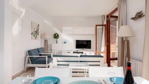 Una sala de estar moderna con sofá, televisión y comedor con mesa para dos.