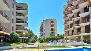Un moderno edificio de apartamentos con piscina, rodeado de céspedes y árboles bien cuidados.