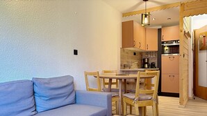 En kompakt opholdsstue med en sofa, et lille bord og et tekøkken.