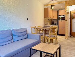 A compact living space with a sofa, a small table, and a kitchenette area.