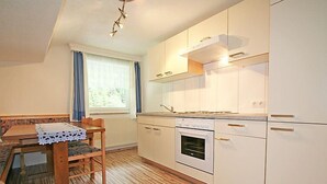 Cocina moderna con armarios blancos, horno empotrado y comedor con mesa y sillas de madera.