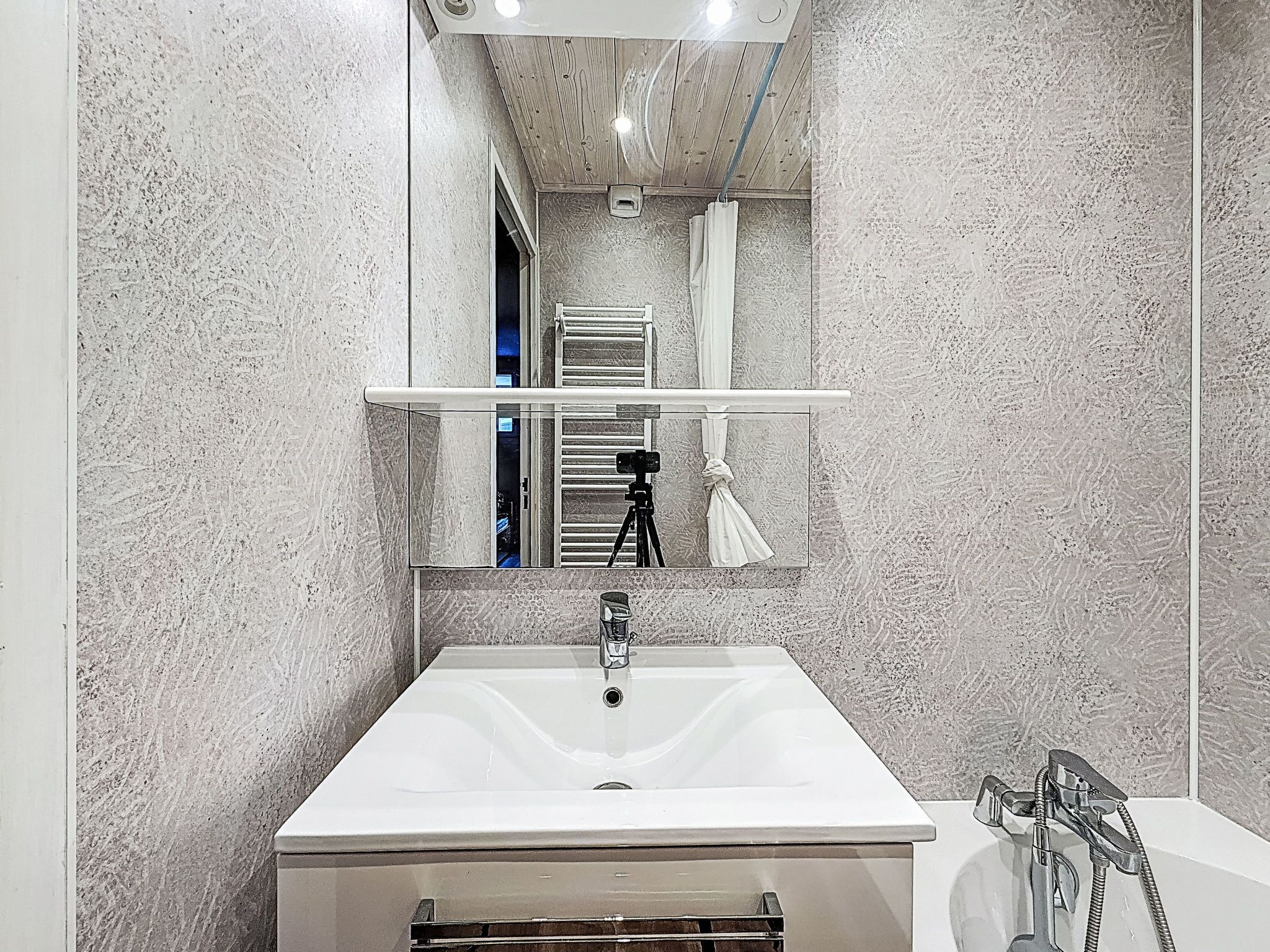 A bathroom with a large mirror, a white sink, a towel rack, and a shower.
