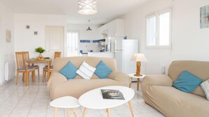 A modern living room with a beige sofa, two white round tables, and a dining area with a wooden table and chairs. - Patguyflor by Interhome (Mimizan)