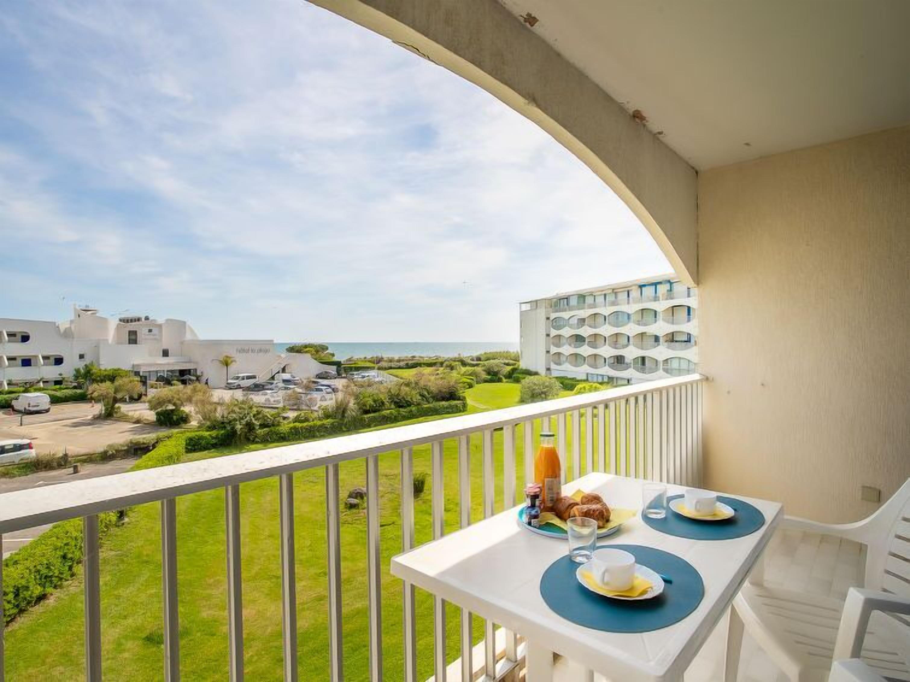 En balkong med ett bord dukat för frukost, med utsikt över ett bostadsområde och havet.