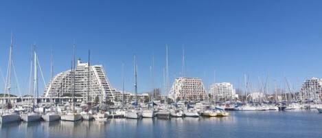 A marina with multiple boats docked, surrounded by modern buildings with a unique architectural design.