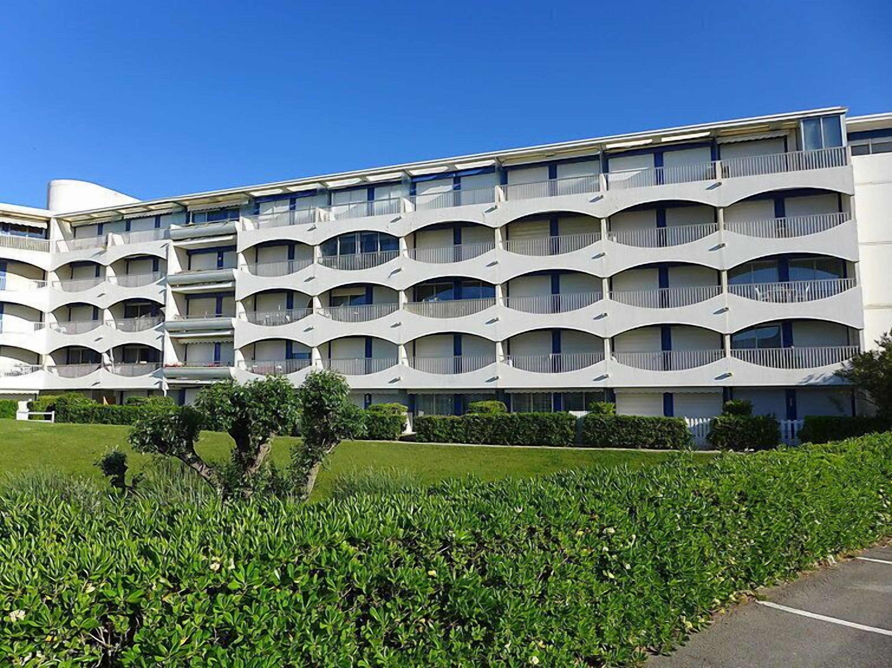 Een modern hotel met een opvallende, golvende gevel, meerdere balkons en een verzorgd gazon ervoor.